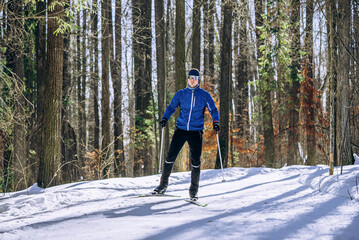 Man actively cross-country skiing on a groomed trail in a tranquil winter forest, engaging in a healthy outdoor workout and enjoying the snowy natural landscape