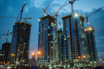 high buildings under construction with cranes and illuminating at night