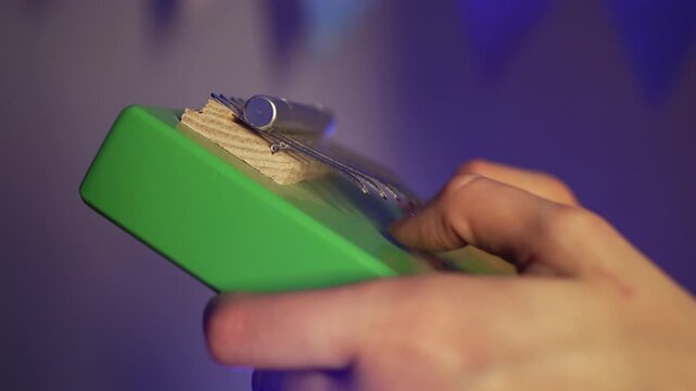 Musician plucking delicate tines of green kalimba, creating soothing melodic sounds with graceful finger movements during intimate musical performance
