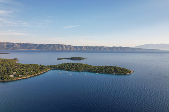 Aerial view of islands cloaked in emerald forests meet the tranquil azure waters, framed by distant mountains under a serene sky, Jelsa, Split-Dalmatia County, Croatia.