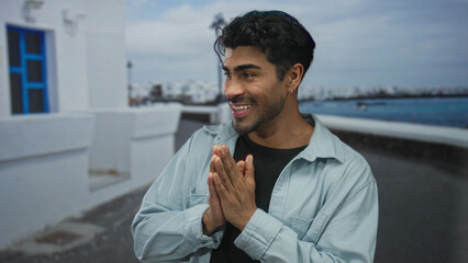 Young man pressing cheeks with both hands and puckering lips beside a white wall on a seaside...