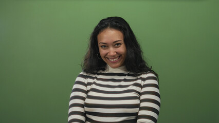 Obraz premium Woman smiling, showing teeth in studio against green wall and striped turtleneck; confidence warmth approachability.