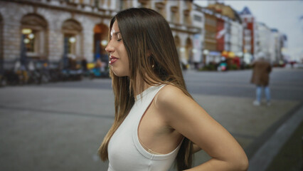 Woman leaning in white tank top with arm bent and hands on hips on busy city street lined with...