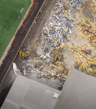 Aerial view of a construction site with heavy machinery amid the rubble, a stark contrast to the adjacent green field, Brooklyn, New York, United States.