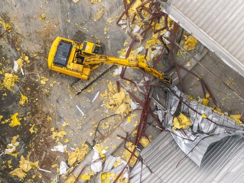 Aerial view of a yellow excavator amidst debris and destruction, tearing through the remains of a collapsed structure, Brooklyn, New York, United States.