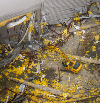 Aerial view of a demolition site where a yellow excavator tears through a crumbling building, its raw edges exposed against the urban landscape, Brooklyn, New York, United States.