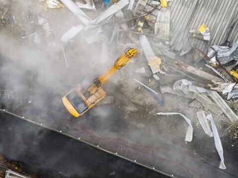 Aerial view of a yellow excavator tearing through the remains of a building amidst a cloud of dust and debris, Brooklyn, New York, United States.