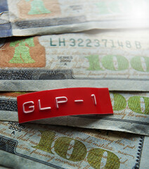 Red GLP-1 label on assorted one hundred dollar bills -- drug price concept