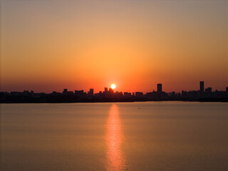 Obraz premium The sun sets over the water, casting a warm glow on the city skyline.