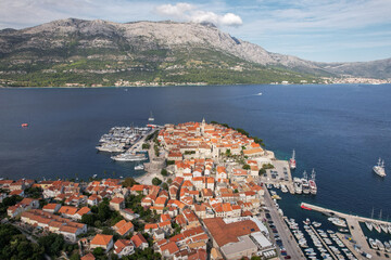 Aerial view of the old town's red rooftops contrasting against the turquoise sea, with the majestic mountains in the backdrop, Korcula, Dubrovnik-Neretva County, Croatia.