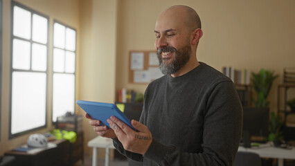 Man using tablet indoors smiling in a bright office setting with plants visible in background emphasizing productivity and digital access in a modern workplace.