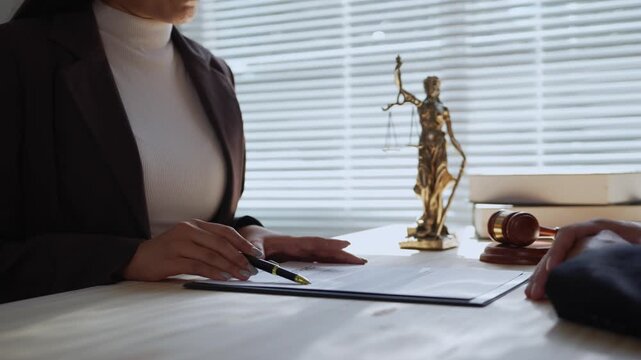 Professional female lawyer explaining legal document terms to a client during a consultation. A gavel and scales of justice statue sit on the desk