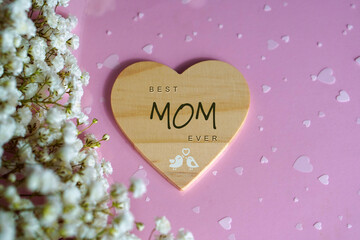 Best mom ever. Message written on a wooden heart against a pink background with white flowers