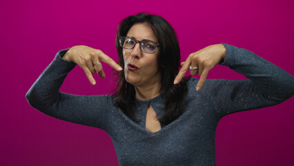Middle aged hispanic woman hands form rock horns gesture while smiling against magenta wall in...