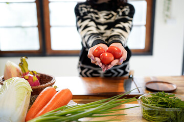 young woman showing tomato standing in kitchen