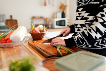 Person chopping green onions on a wooden cutting board in a kitchen.