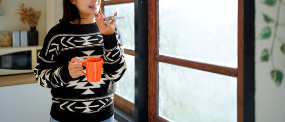 woman using phone voice assistant and holding coffee in morning home kitchen. Relax retirement lady typing smartphone, online network website