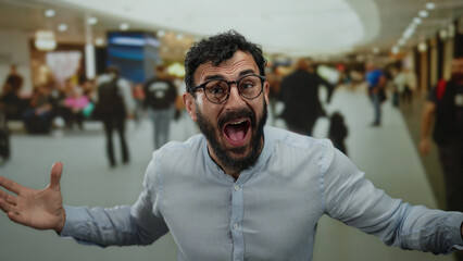 Hispanic man with beard shouting excitedly in bustling shopping center with blurred background of...