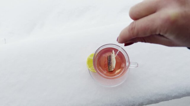 Hand dipping teabag over a tea cup outdoors on winter snow