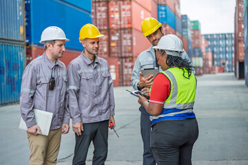 Diverse logistics team discussing shipment plan in shipping container yard. Supervisor briefing industrial workers about cargo export schedule at commercial freight terminal port.