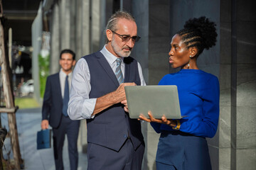 Group of diverse business professionals discussing a project outside an office building. The scene captures leadership, teamwork, strategic planning, and corporate communication in natural daylight.