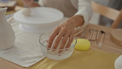 Young woman wearing apron with hands shaping clay on potter wheel in studio; creativity focus craftsmanship calm.