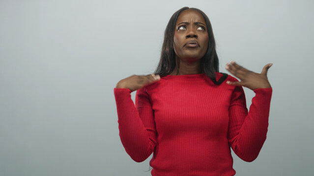 Black woman gesturing with hands, palms up and shrugging shoulders in studio against neutral grey wall, mid motion wearing red sweater; frustration.