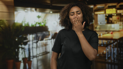 Woman smiling and offering cupped hands gesture in building restaurant interior wearing black...
