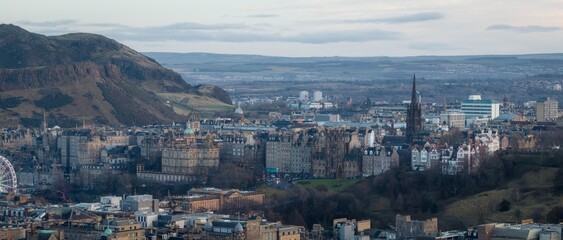 Aerial view of Edinburgh's skyline with the iconic spire piercing the cloudy sky, and Arthur's Seat looming over the historic buildings, Edinburgh, Scotland, United Kingdom.