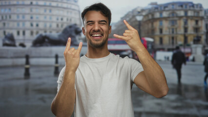 Young hispanic man outdoors making rock gesture with happy expression in urban setting featuring...