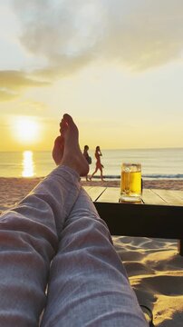Man relaxing on Thailand sandy beach at sunset with beer drink on table