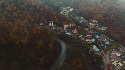 Aerial view of a winding road cutting through the muted autumn hues of the forest, leading to the clustered buildings of the village, Asalem, Gilan Province, Iran.