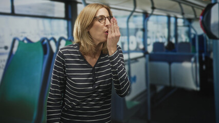 Fototapeta premium Woman covering mouth with hand by bus seat, wearing glasses and striped top on street; surprise curiosity playfulness.