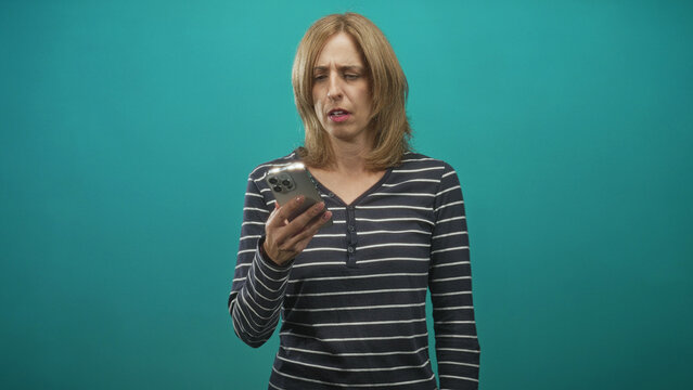 Woman in striped shirt holding smartphone to ear, tilting head and rolling eyes in teal studio; frustration fatigue.