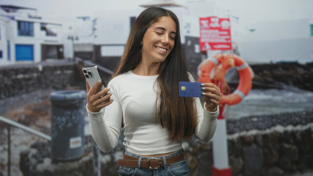Young woman holding smartphone and creditcard, smiling and showing card in studio; confidence convenience. - Powered by Adobe