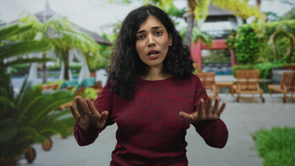 Woman with hand on chest and palms raised at resort pool practicing slow breath gesture, eyes closed and relaxed; calm reflection.