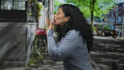 Young arab brunette woman smiling, face visible, speaking and slightly turning head while standing on a sunny city street with parked bike and cars; confidence casual moment.