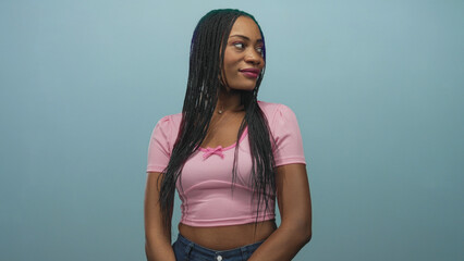 Black woman in pink crop top showing midriff pointing thumb over shoulder in studio; confident playfulness.
