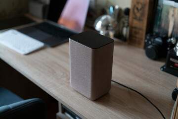 A speaker is placed on a wooden desk with a laptop and camera in a workspace setting