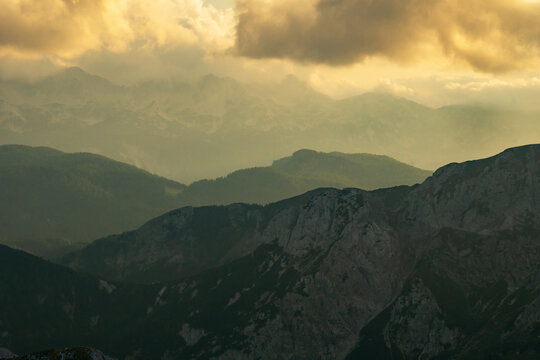 Aerial view of the rugged Julian Alps under a sky brushed with gold, a symphony of light and shadow over the mountainous terrain, Tosc, Radovljica, Slovenia.