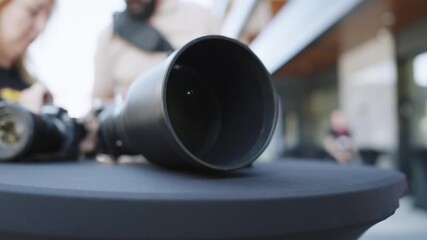 Close-up View of telephoto large camera lens sitting on table with background of video and photo operators