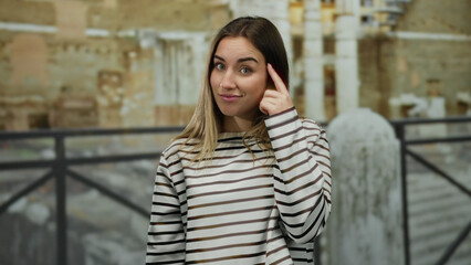 Fototapeta premium Woman standing among ancient roman ruins in rome, smiling confidently with a thoughtful expression, wearing a striped shirt, surrounded by historic architecture.