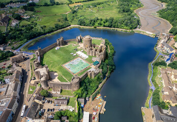 Aerial view of Pembroke Castle, with its formidable stone walls reflected in the still waters surrounding it, a vibrant green lawn within, Pembroke, Pembrokeshire, Wales.