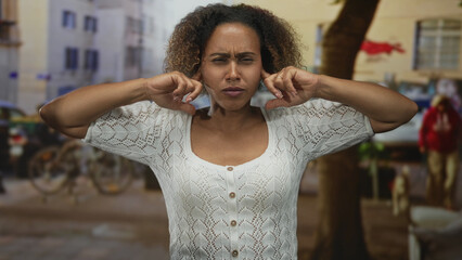 Woman pressing fingers into ears on street with bicycles and buildings visible; frustration sensory overload.