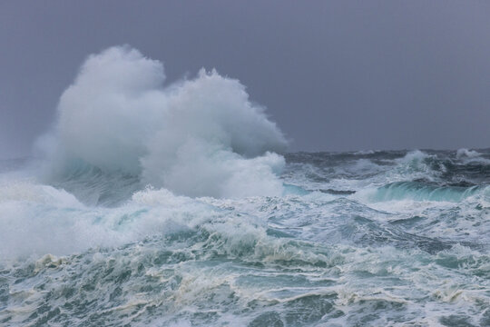 View of frothy, churning waves crash and collide under a moody, overcast sky, a powerful display of nature's raw energy, Sorvagur, Vagar, Faroe Islands.