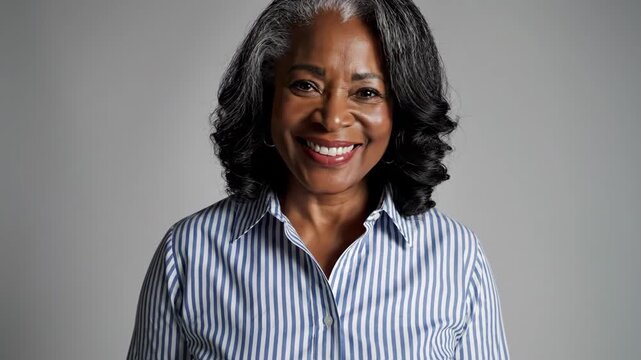 Elegant Mature Woman Portrait - A beautiful mature woman with gray hair smiles warmly in a studio portrait. She is wearing a striped button-down shirt and looks directly at the camera.