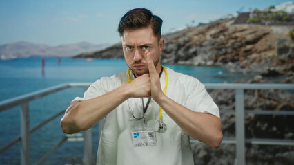 Fototapeta premium Young bearded caucasian doctor with stethoscope making fighting gesture by seaside, blending medical professionalism with an outdoor coastal setting on a sunny day at the beach.