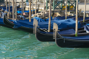 Row of gondolas docked along a canal in Venice, Italy. Traditional metal prow ornaments - ferro © Pavel