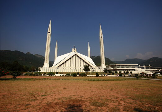 View of Faisal Mosque's stark white marble contrasts against the warm browns of the dry lawn under a clear sky, Islamabad, Islamabad Capital Territory, Pakistan.