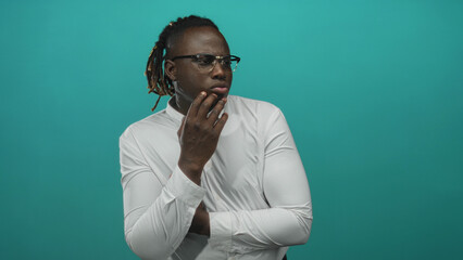 Man with hand on chin pensive pose in studio with teal backdrop and white shirt; thoughtful...